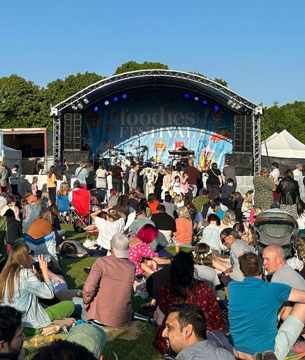 An Arc Truss Stage set up for a band performance in the middle of a field for a festival with a busy audience around the front and a bright blue sky above.