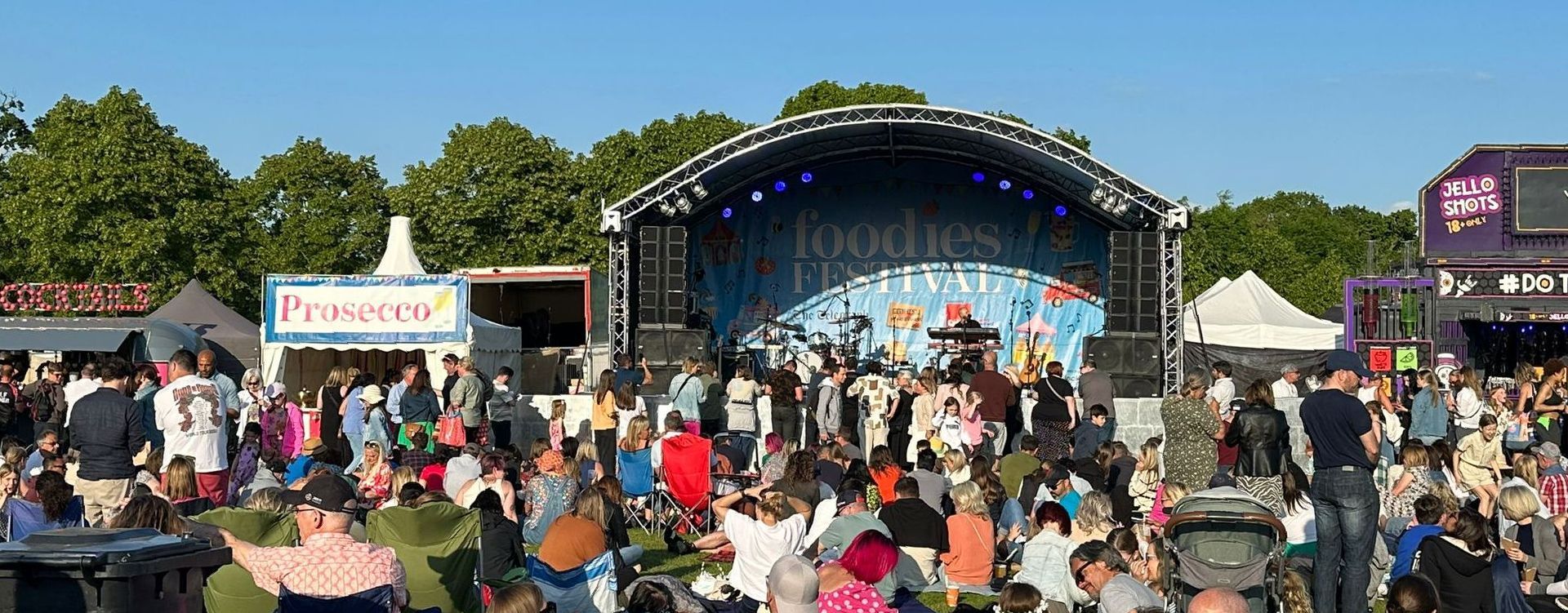 an arc truss stage at the Foodies event. There's a large audience in front of the stage and stalls either side of it.