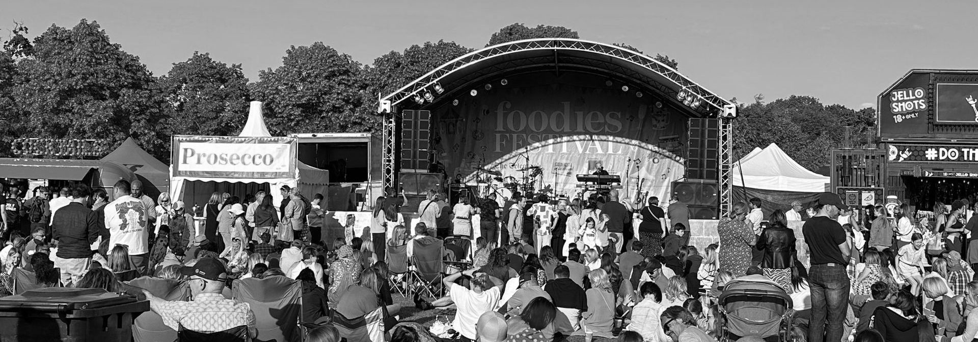 A black and white photo of an arc truss stage with a large audience waiting for a band to play