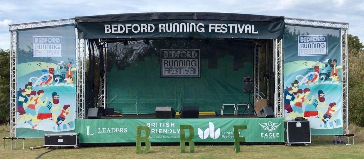 Trailer stage with PA wings set up for an event in a field.