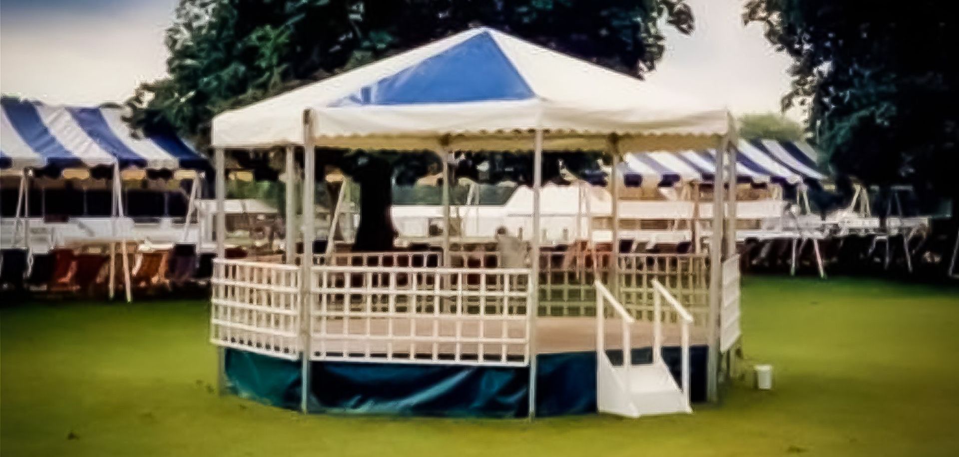 A bandstand in a green field with a blue skirt and blue and white canopy. 