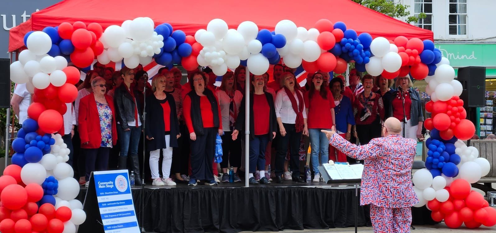 A choir performing on a modular stage with red canopy and red, white and blue balloons around the outside. 