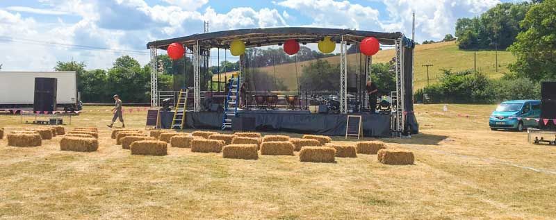 Extra large trailer stage set up in a burnt grass field with hay bails set up in front of it.