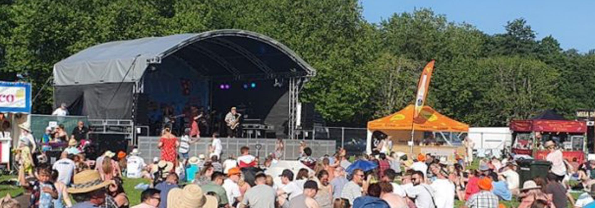 A large arc truss stage set up with a band performing on it and a large audience watching on