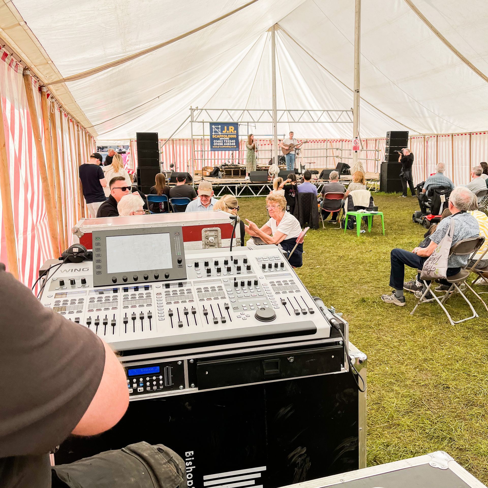A modular stage set up in a marquee with a duo performing on it. In the foreground a mixing desk