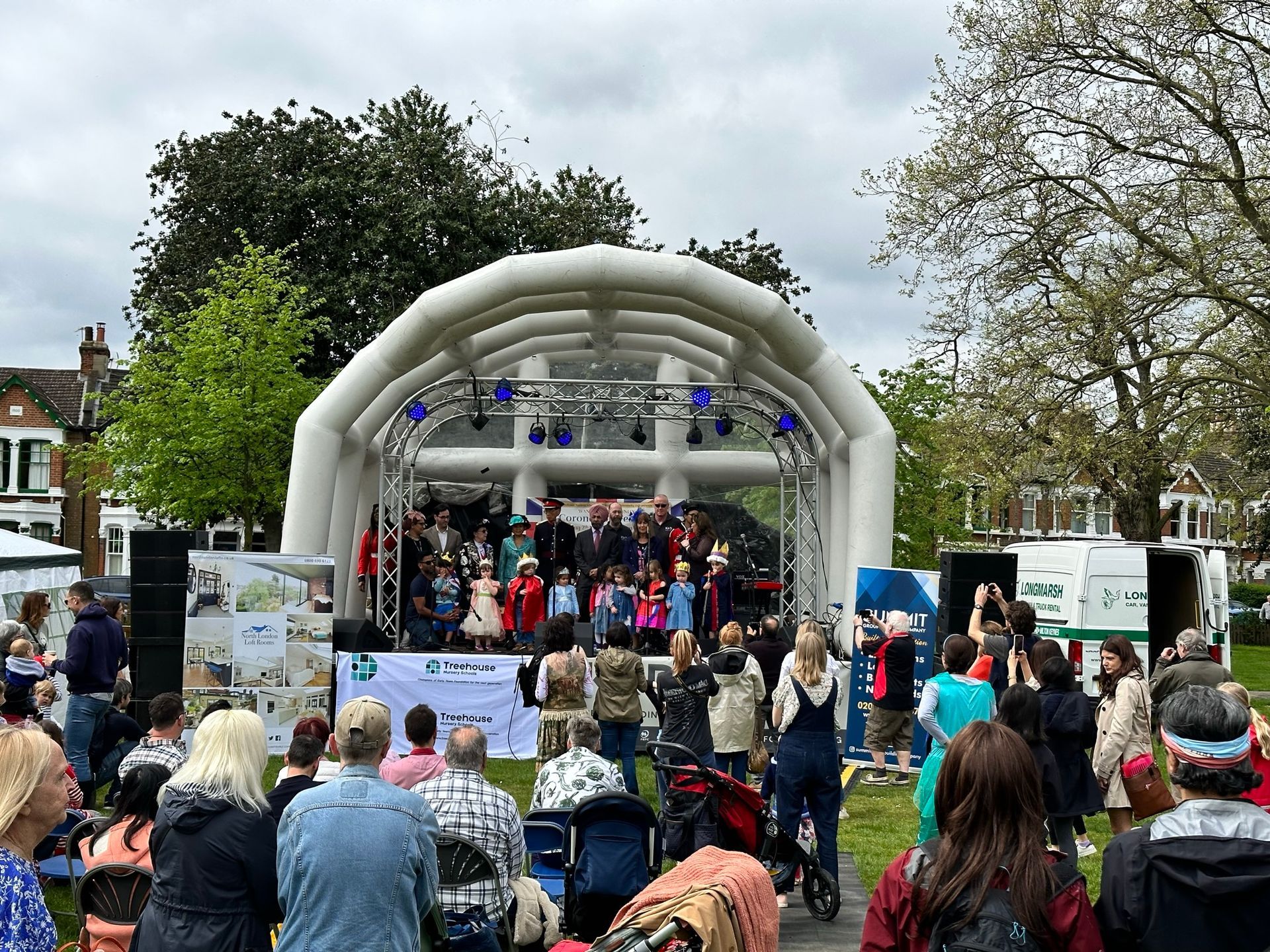 Inflatable roof trailer stage with a children's choir performing on it and a large audience in front.
