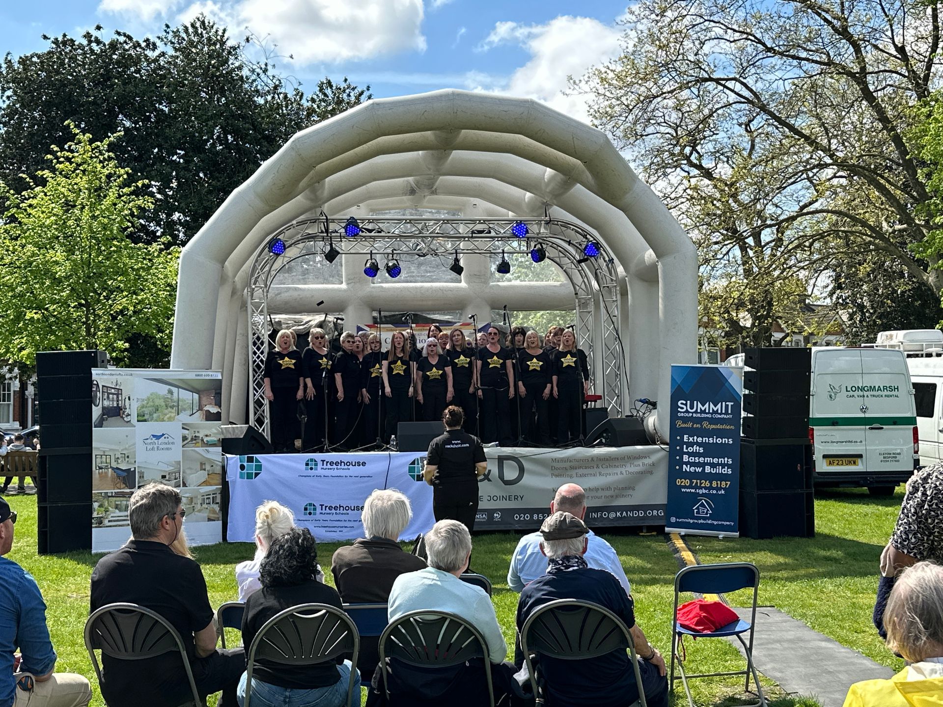 an inflatable roof stage with a choir performin on it and an audience sat in front.