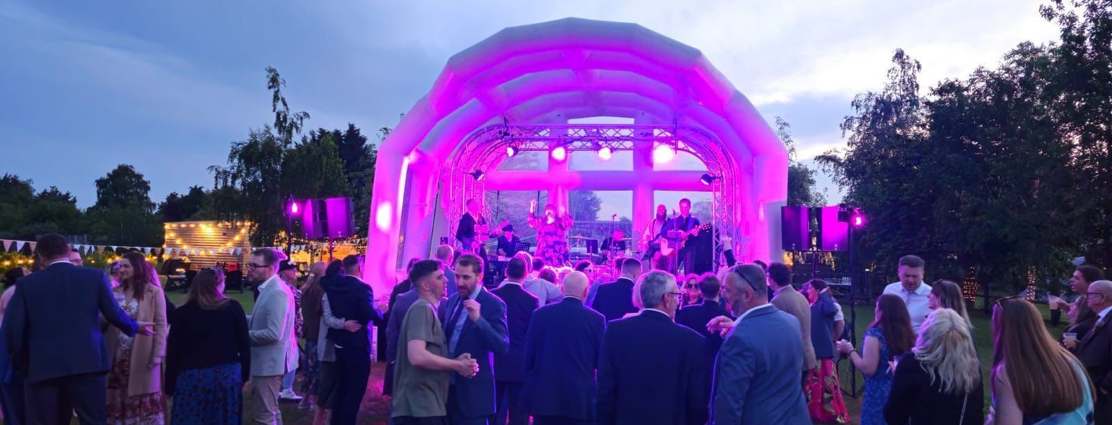 An inflatable roof stage at a festival wedding, with a band playing and an audience watching and dancing