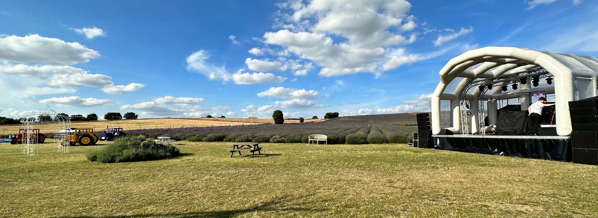 An inflatable trailer stage set up in a field with lavender in the background, the sky is blue with a few fluffy clouds