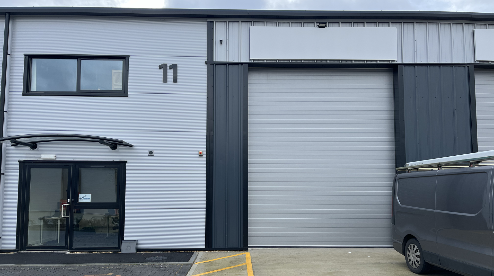 A grey warehouse, with the number 11 on the front, a normal door and a large sliding door to the right.