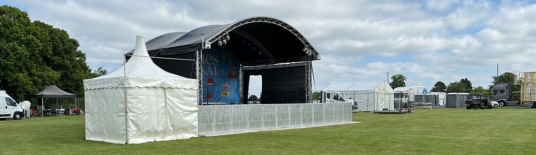 An arc truss stage set up in a field with crowd barriers and other marquees surrounding it