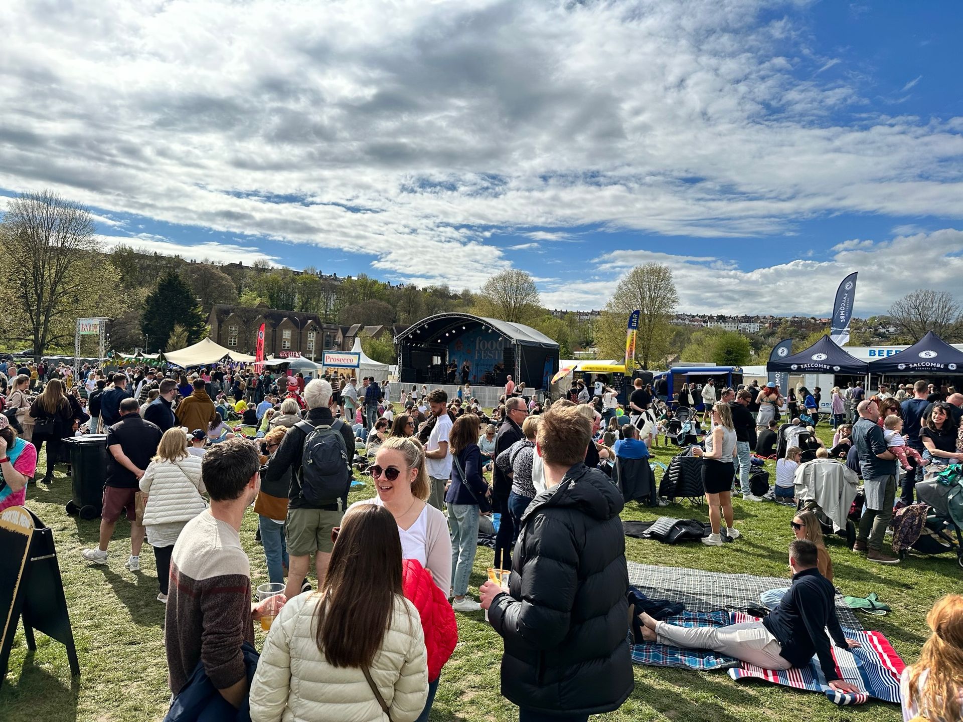 Long shot of the arc truss stage in the middle of a field with lots of people around it.