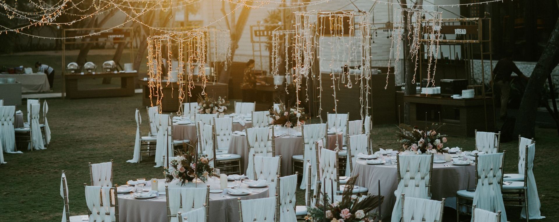 an outdoor wedding with chairs drapped in white and lights hanging between the trees