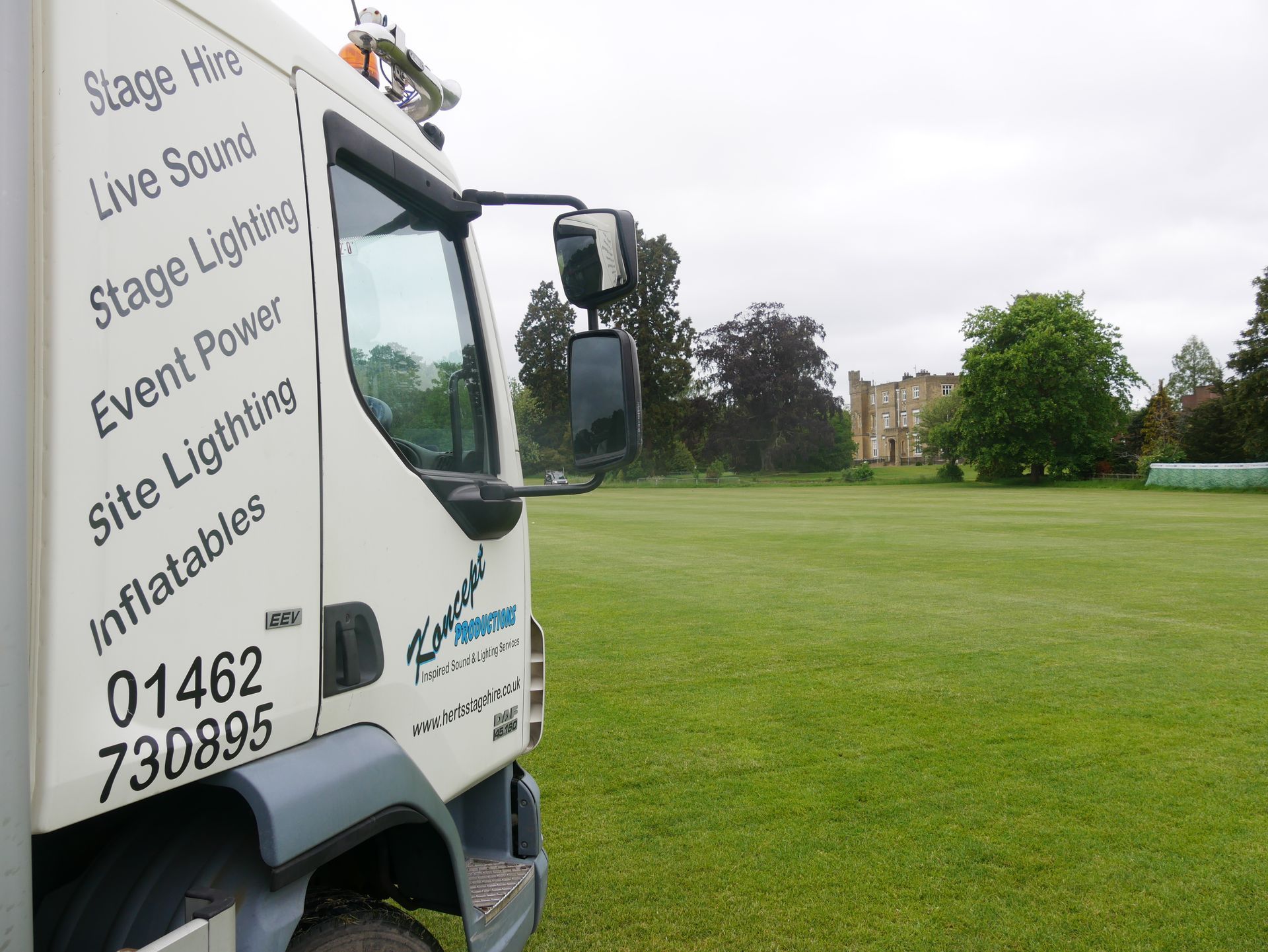 The koncept productions lorry to the left of a field with a manor house in the background.