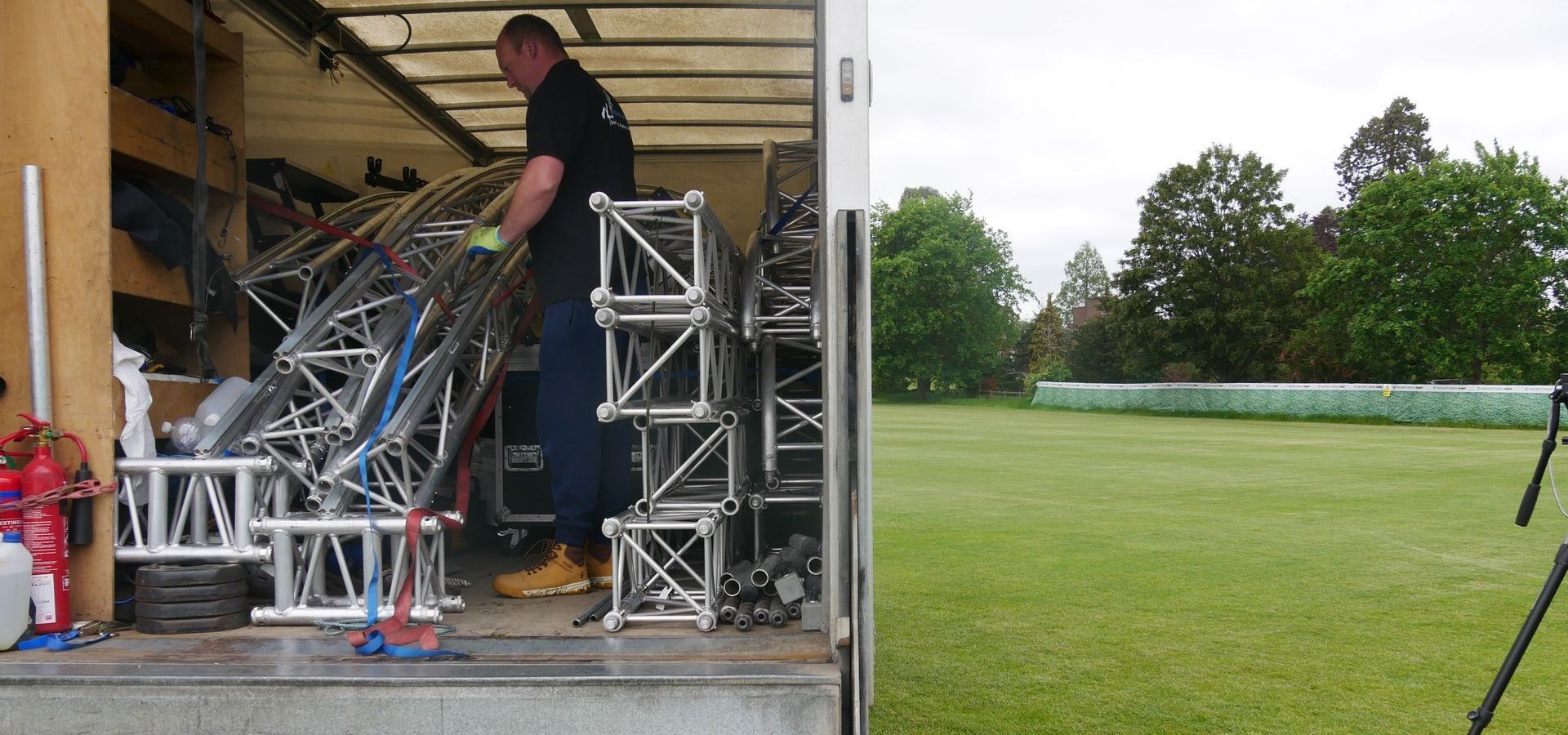 The back end of a lorry is open with stage pieces and equipment inside, a member of the crew is standing amongst it.