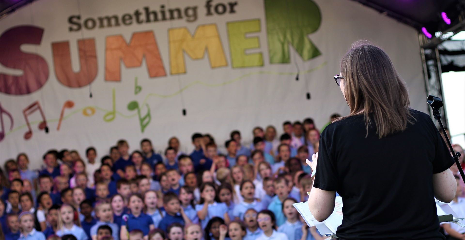 something for summer at shuttle worth. A kids choir performing on an arc truss stage with a conductor in the foreground