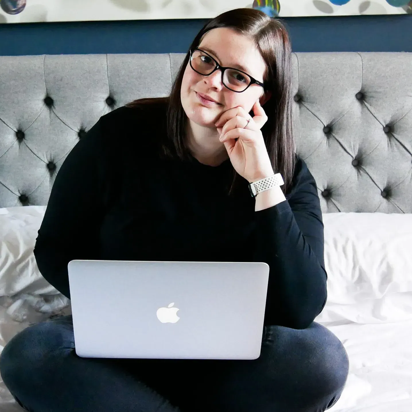 a photo of Sophie working on her laptop in a black jumper and jeans. She has dark hair and wears glasses