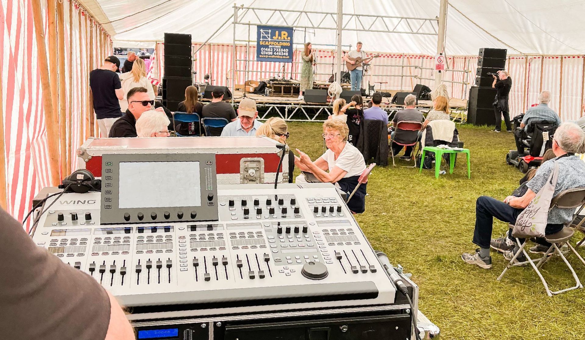 A modular stage set up in a marquee with a duo performing on it. In the foreground a mixing desk