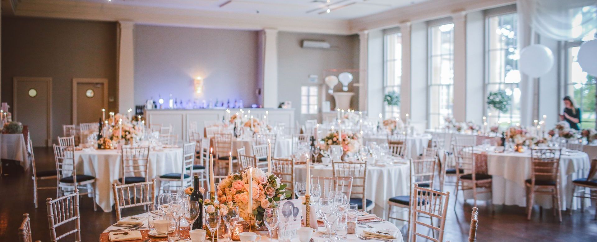 A wedding venue set up for a reception with round tables and chairs, candles and flowers on top and mood lighting