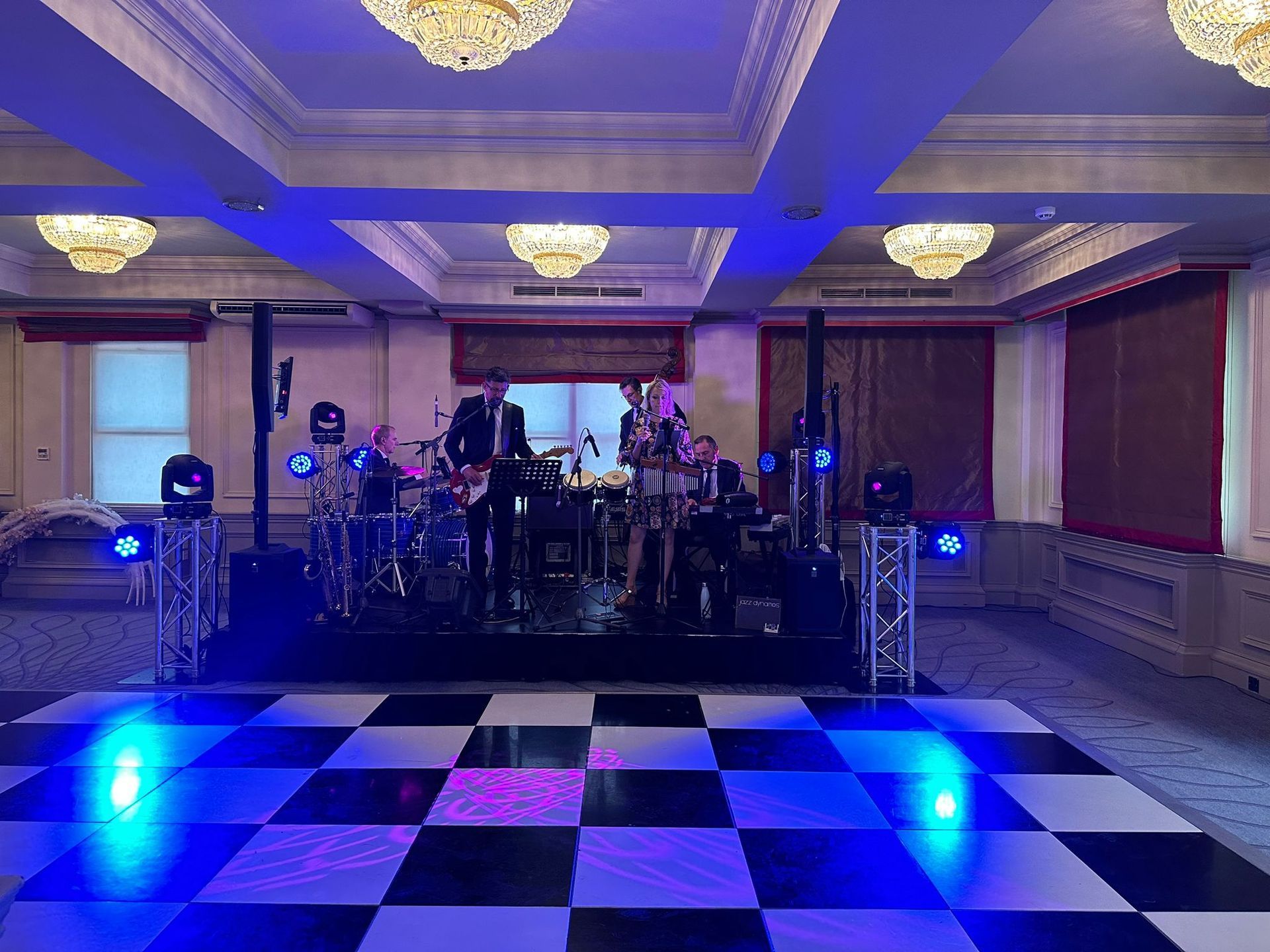 A wedding band on a stage with a chequer board dance floor and blue lights