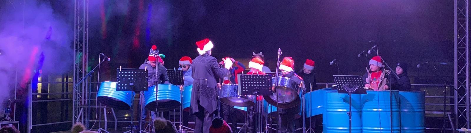 A band of kids playing the steel drums on a stage with christmas hats on.