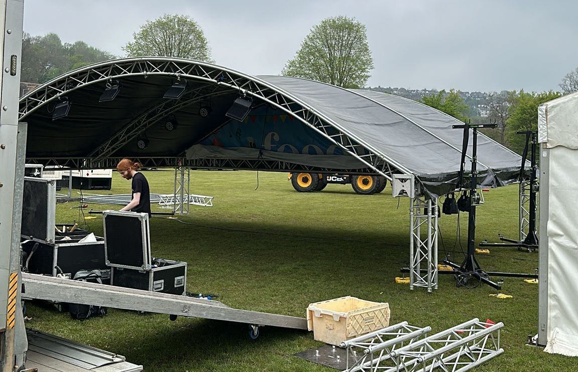 The roof of an arc truss stage mid erection at an event