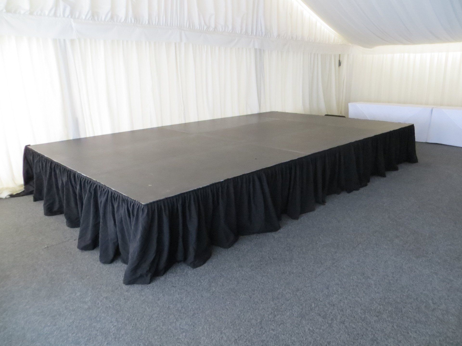 Modular stage set up inside a marquee for a wedding with a black pleated skirt.