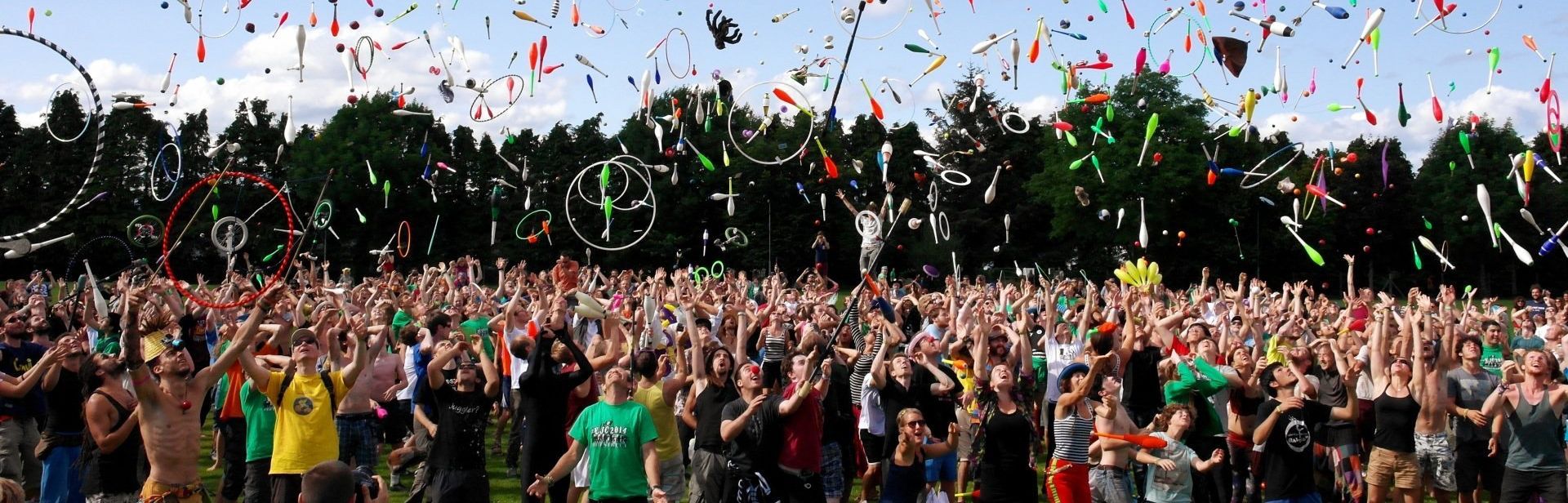 A shot of a large crowd, throwing circus equipment into the air at a family friendly festival.