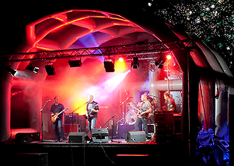 Inflatable roof stage set up for an outdoor event at nighttime with lighting and a band