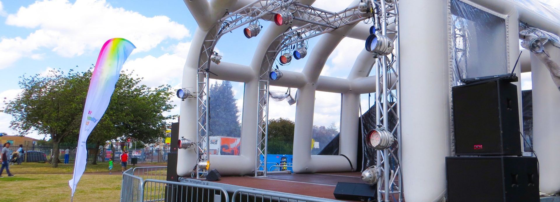 An inflatable stage in a field set up for an event with a multi coloured flag in front and crowd barriers.