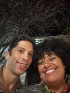 Two smiling people taking a selfie outdoors at night, under a tree.