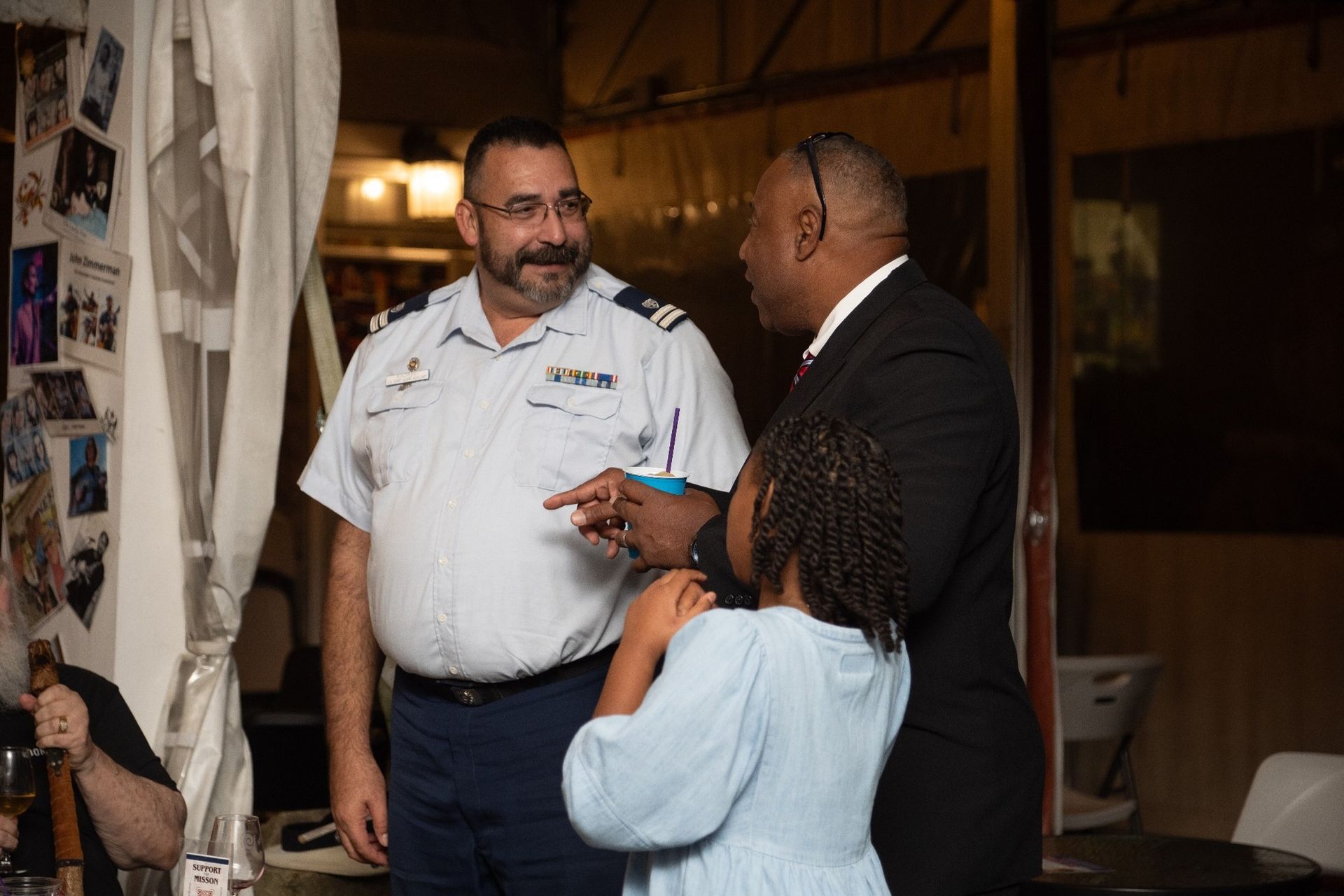 Three people conversing indoors; a uniformed man, a man in a suit, and a child.