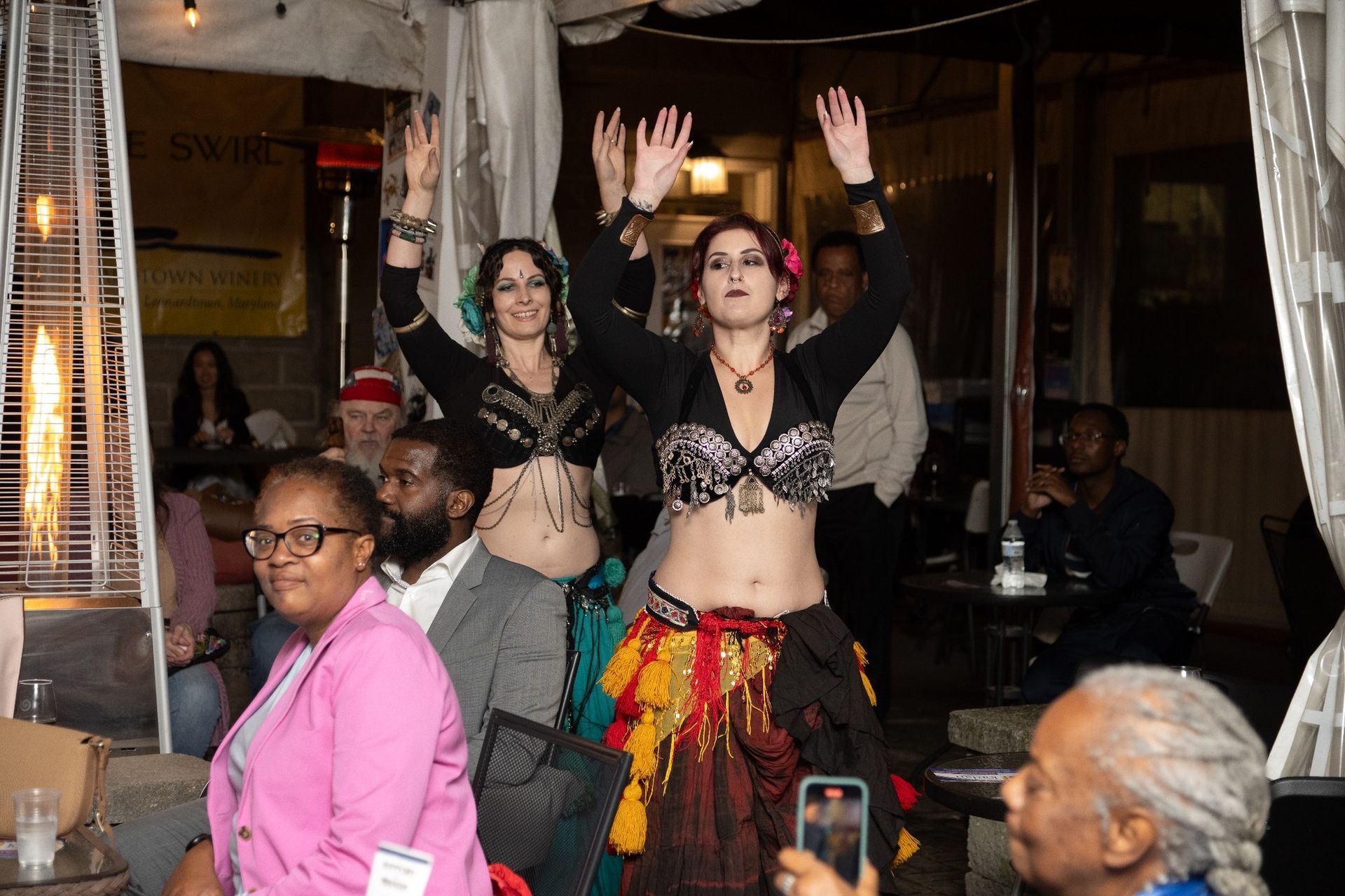 Two belly dancers performing on an outdoor patio with audience members.