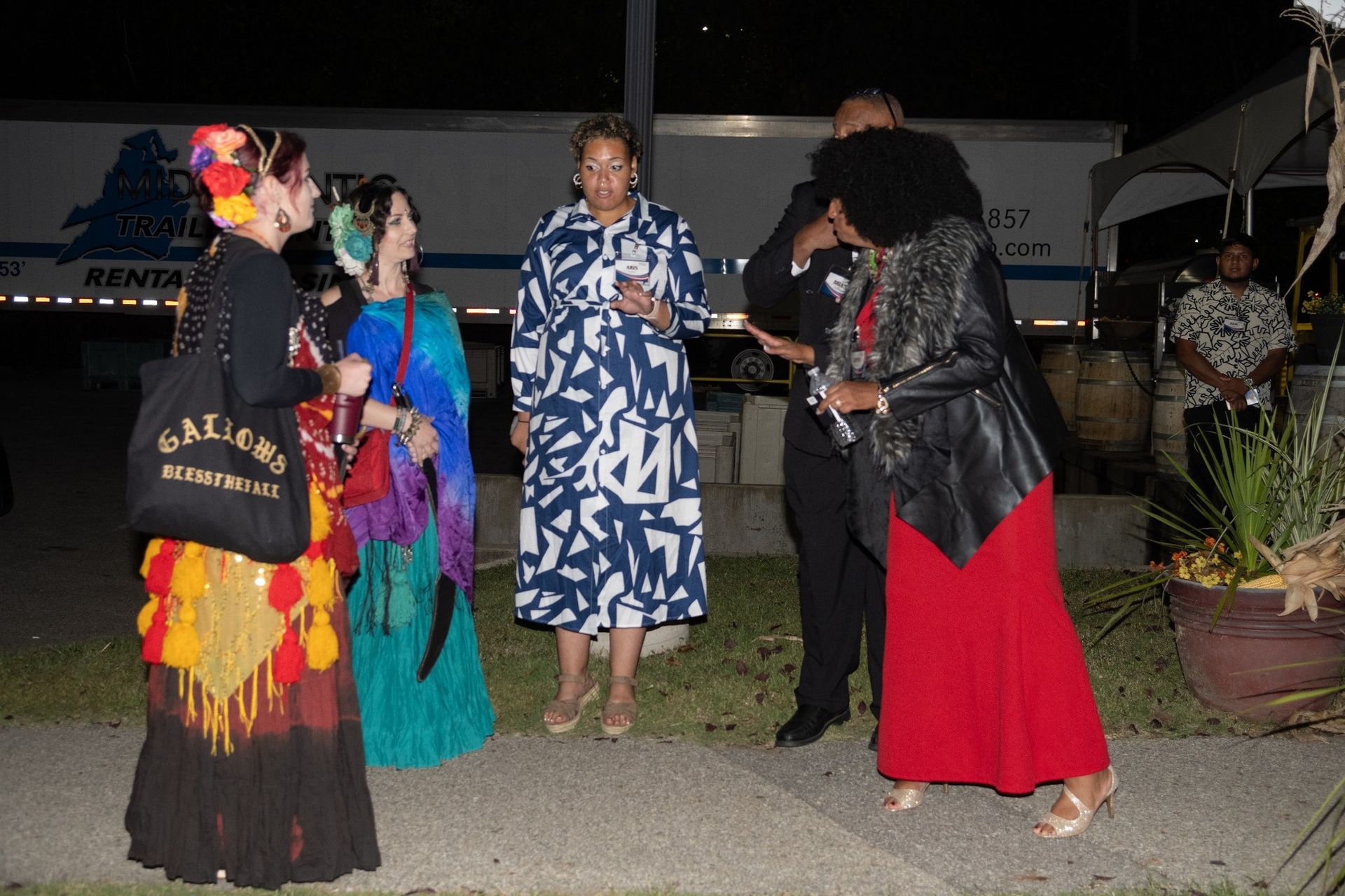 Group of people in colorful outfits socializing outside at night.