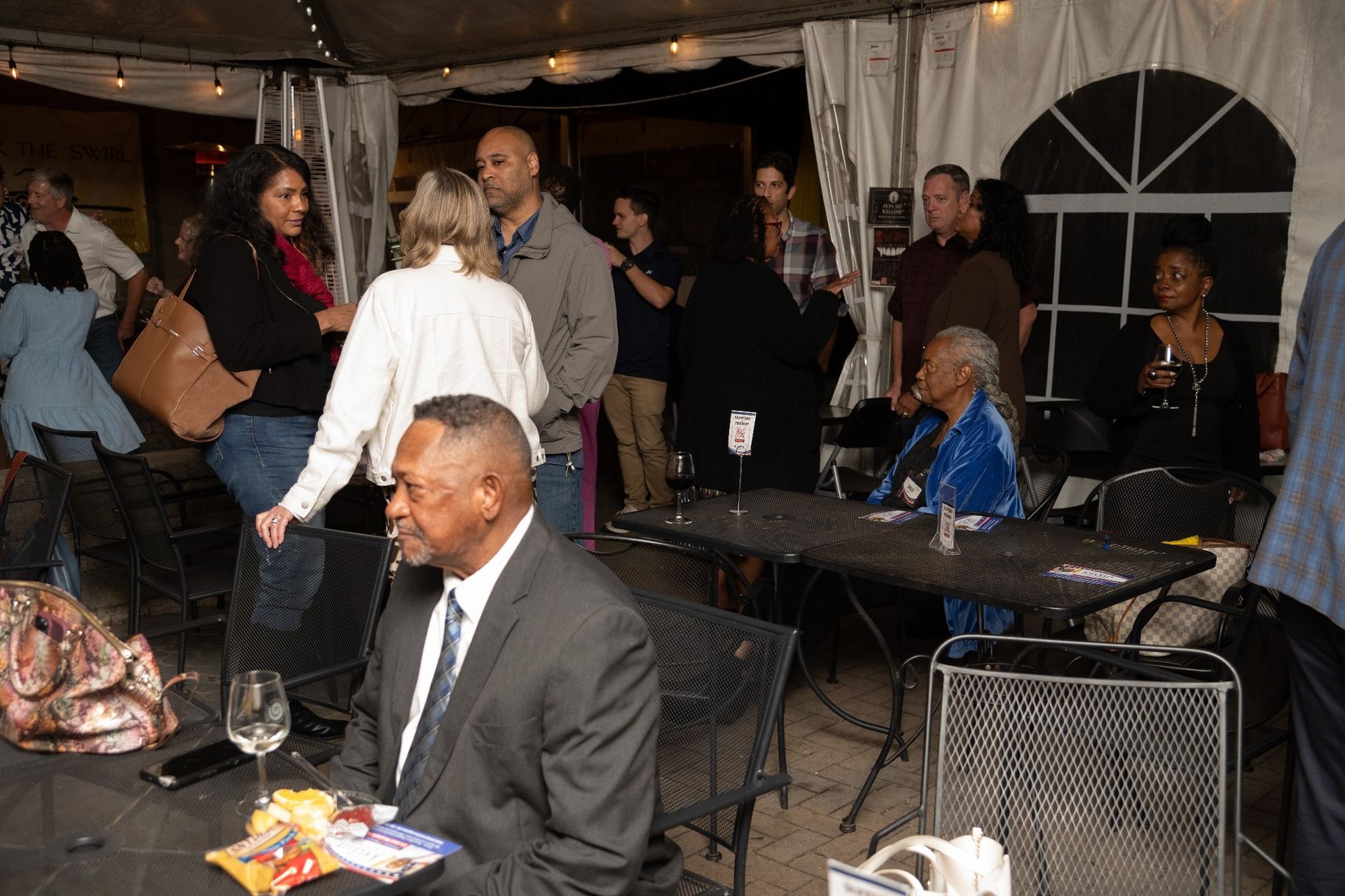 People socializing at an outdoor event with a tent, tables, and drinks.