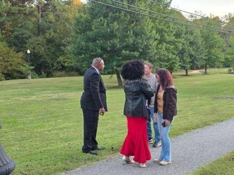 A group of people standing on a paved walkway and grassy area. The person on the left is wearing a suit.
