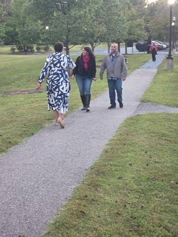 People walking on a path in a park with green grass and trees.