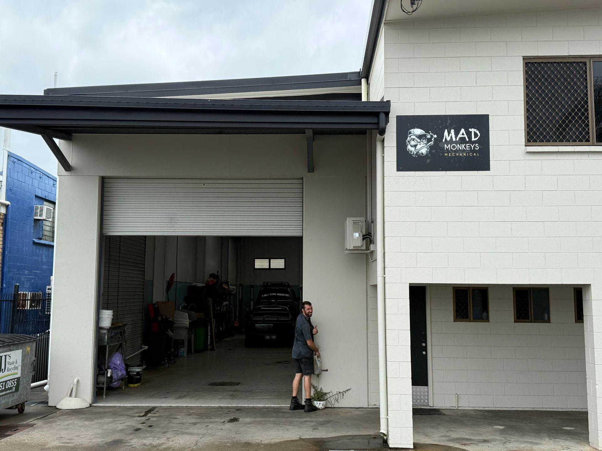 A Person Stands Beside the Open Bay of a White Industrial Building — Mad Monkeys Mechanical in Cairns City, QLD