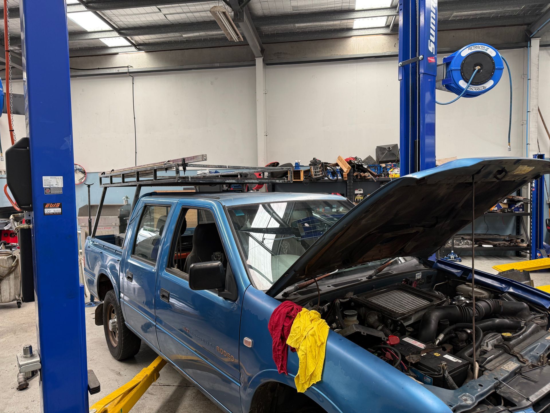 A Blue Pickup Truck With an Open Hood Sits on a Car Lift Inside an Automotive — Mad Monkeys Mechanical in Cairns City, QLD