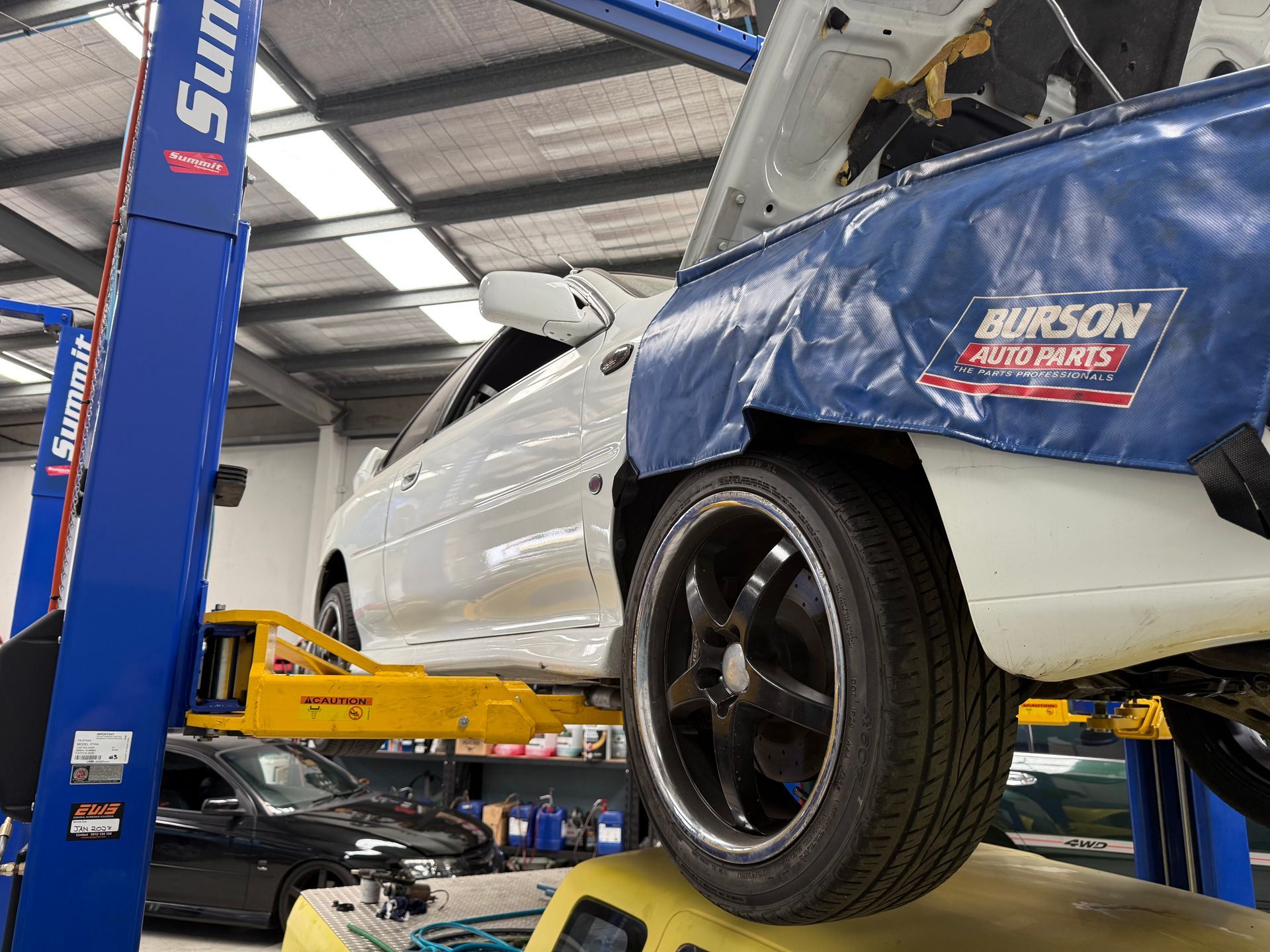 White Car Raised on a Hydraulic Lift in a Garage, With a Cover — Mad Monkeys Mechanical in Cairns City, QLD