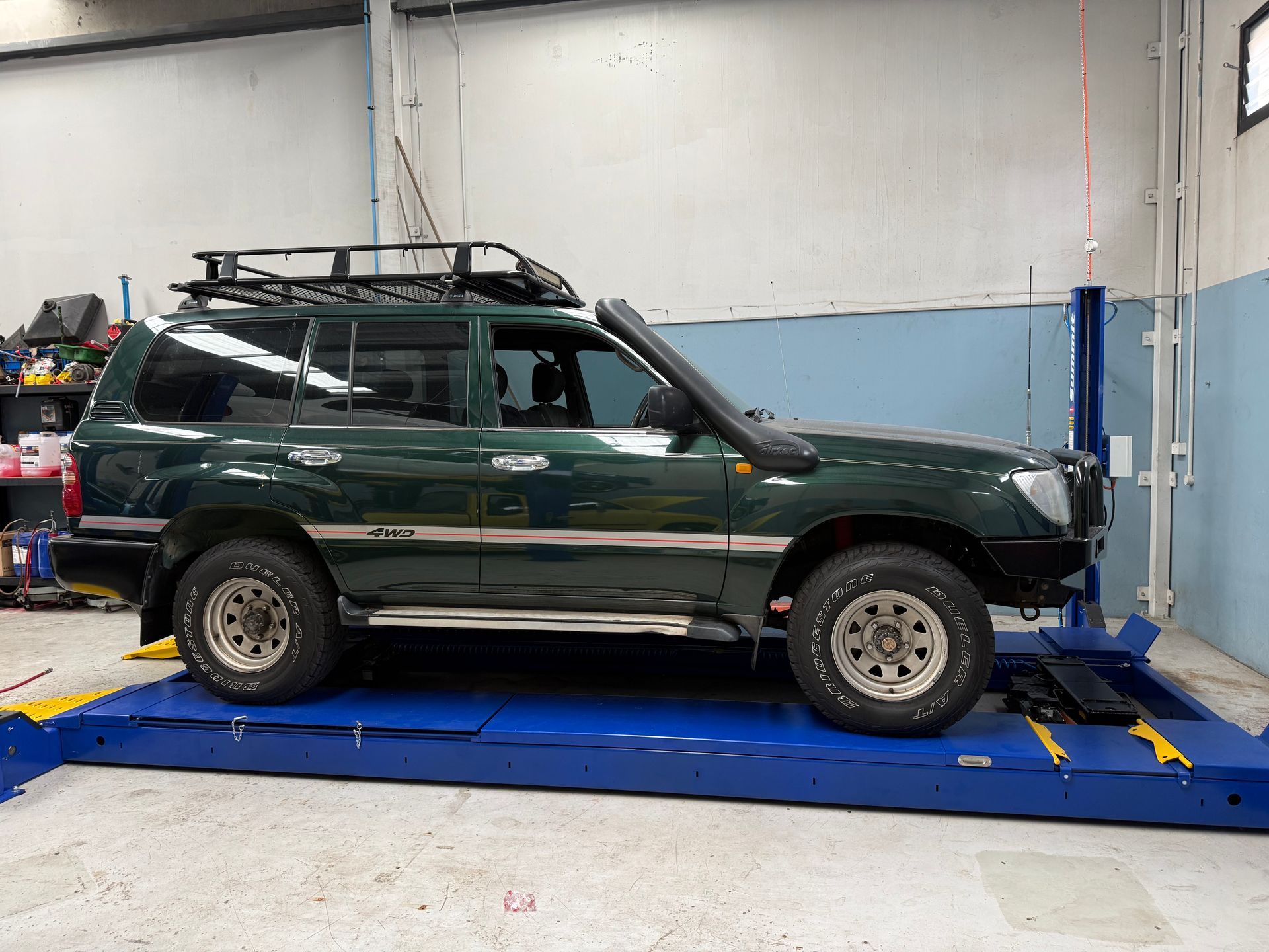 Dark Green SUV with a Roof Rack and Snorkel Parked on a Vehicle Lift in a Garage — Mad Monkeys Mechanical in Cairns City, QLD