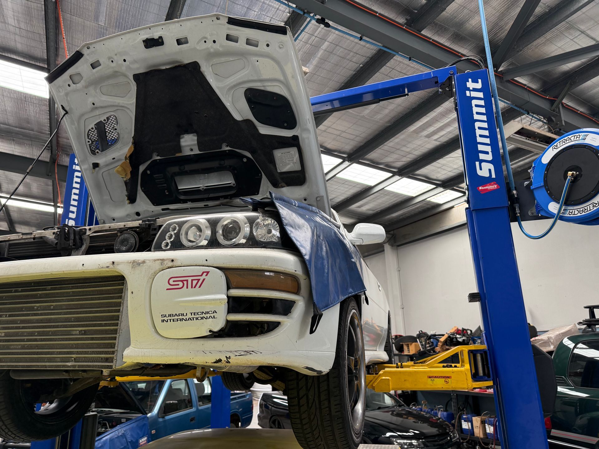 Car With Its Hood Open, Hoisted on a Blue Summit Car Lift a Workshop — Mad Monkeys Mechanical in Cairns City, QLD