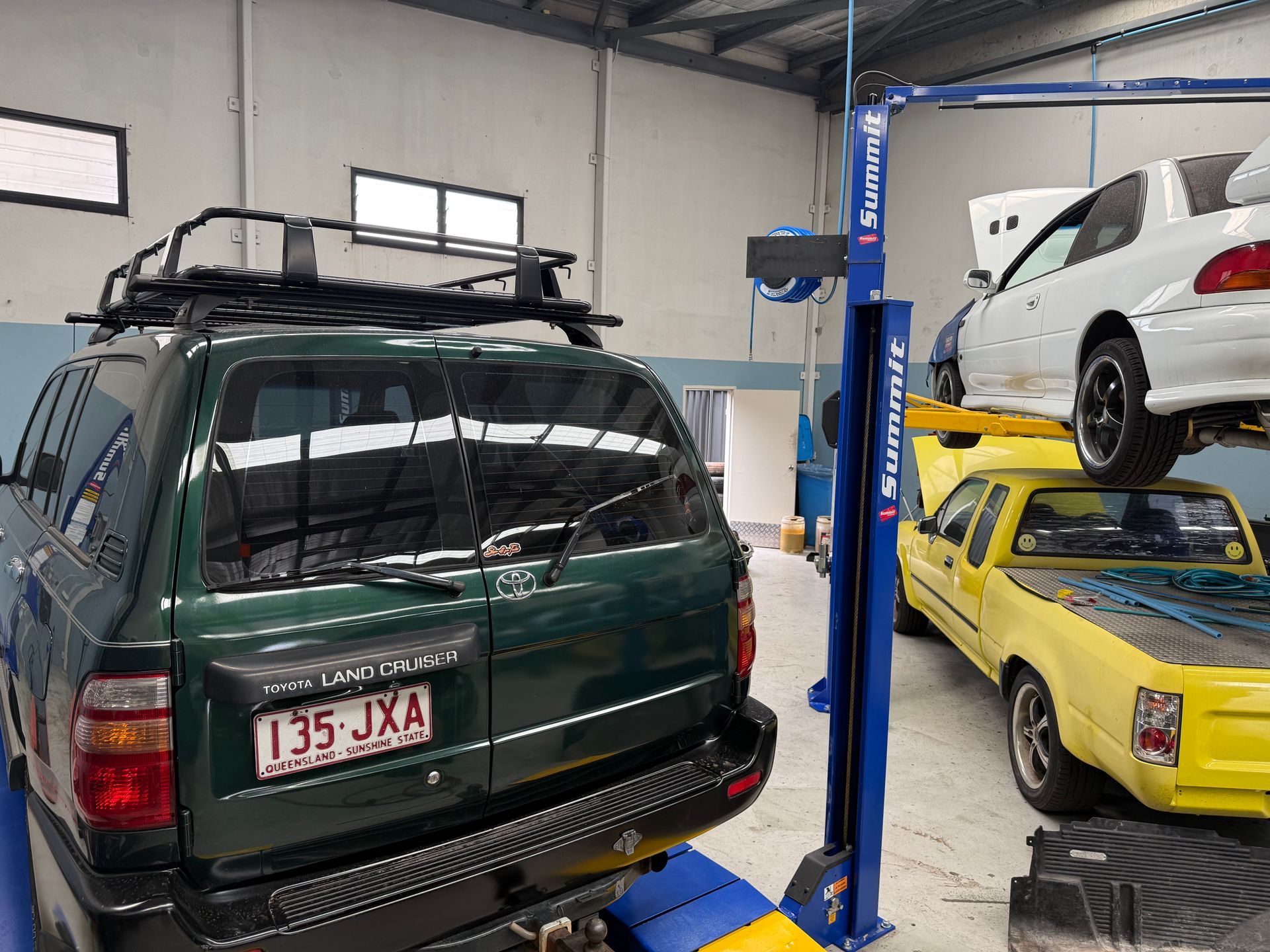 A Dark Green SUV and a Yellow Pickup Truck Inside a Vehicle Repair Shop — Mad Monkeys Mechanical in Cairns City, QLD