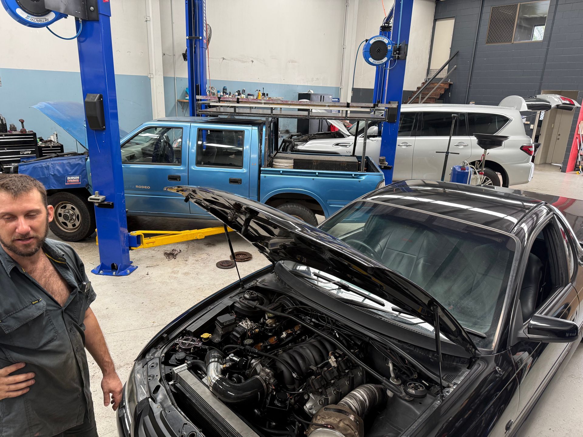 A Man Stands in an Auto Repair Shop Next to a Black Car with Its Hood Open — Mad Monkeys Mechanical in Cairns City, QLD
