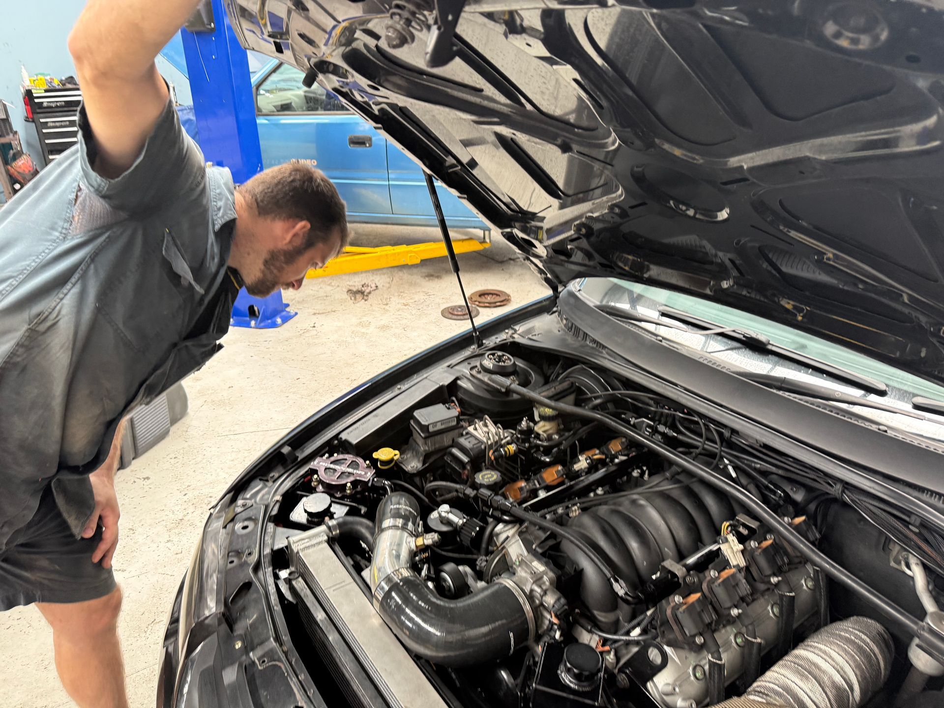 A Mechanic in a Shop Setting Leans Over to Inspect the Open Engine Bay — Mad Monkeys Mechanical in Cairns City, QLD