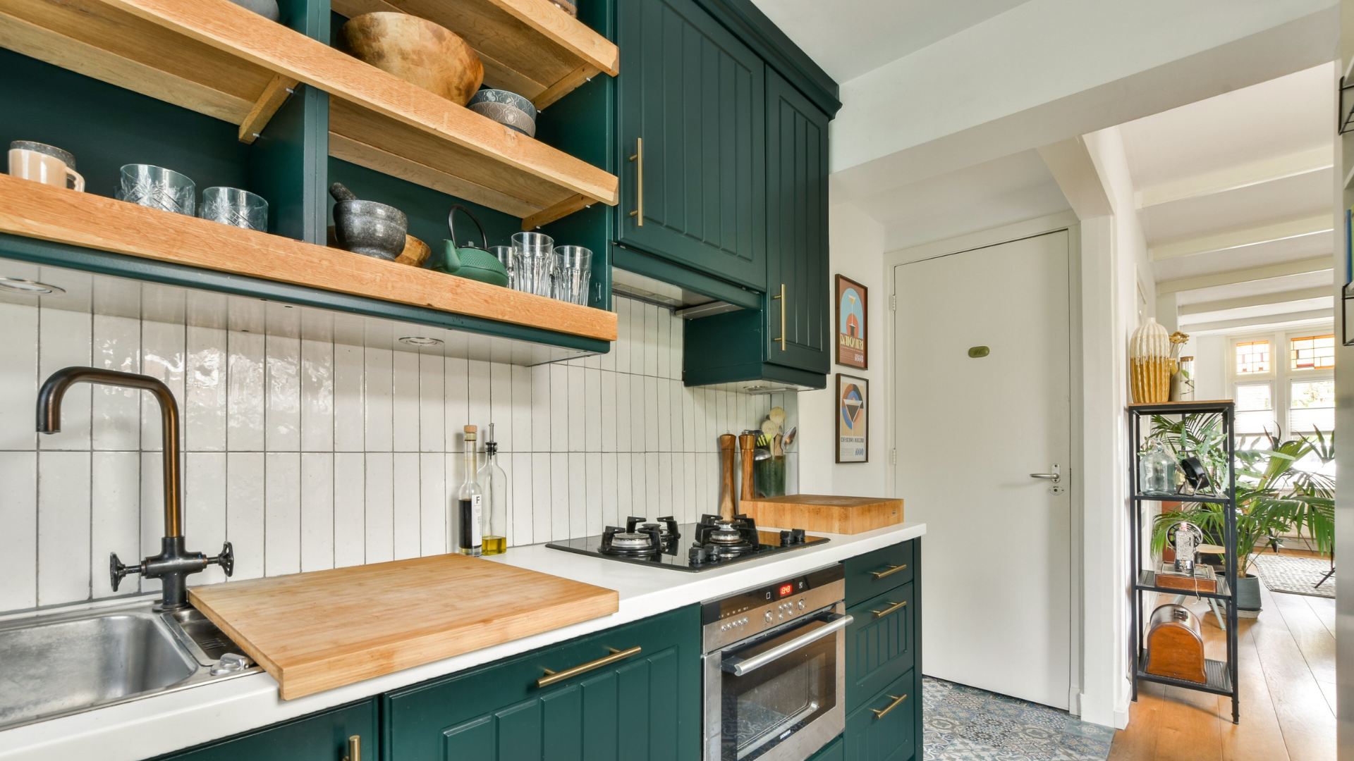 Modern kitchen with teal cabinets, white tile backsplash, open shelves, and a view into a bright hallway.