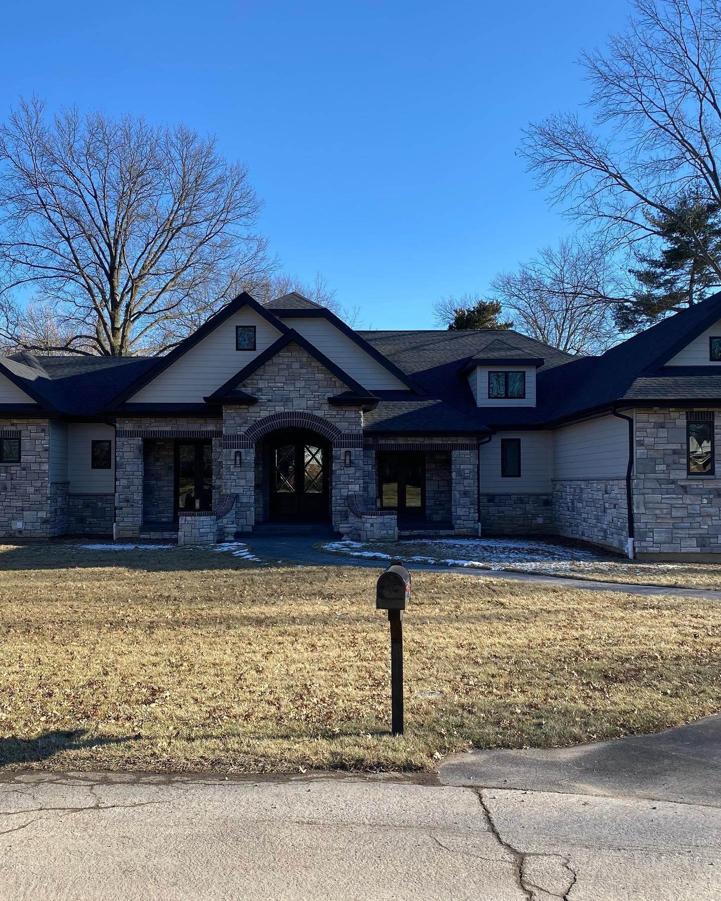 A stone-clad house with a dark roof, on a sunny day. A mailbox stands in front of the lawn.