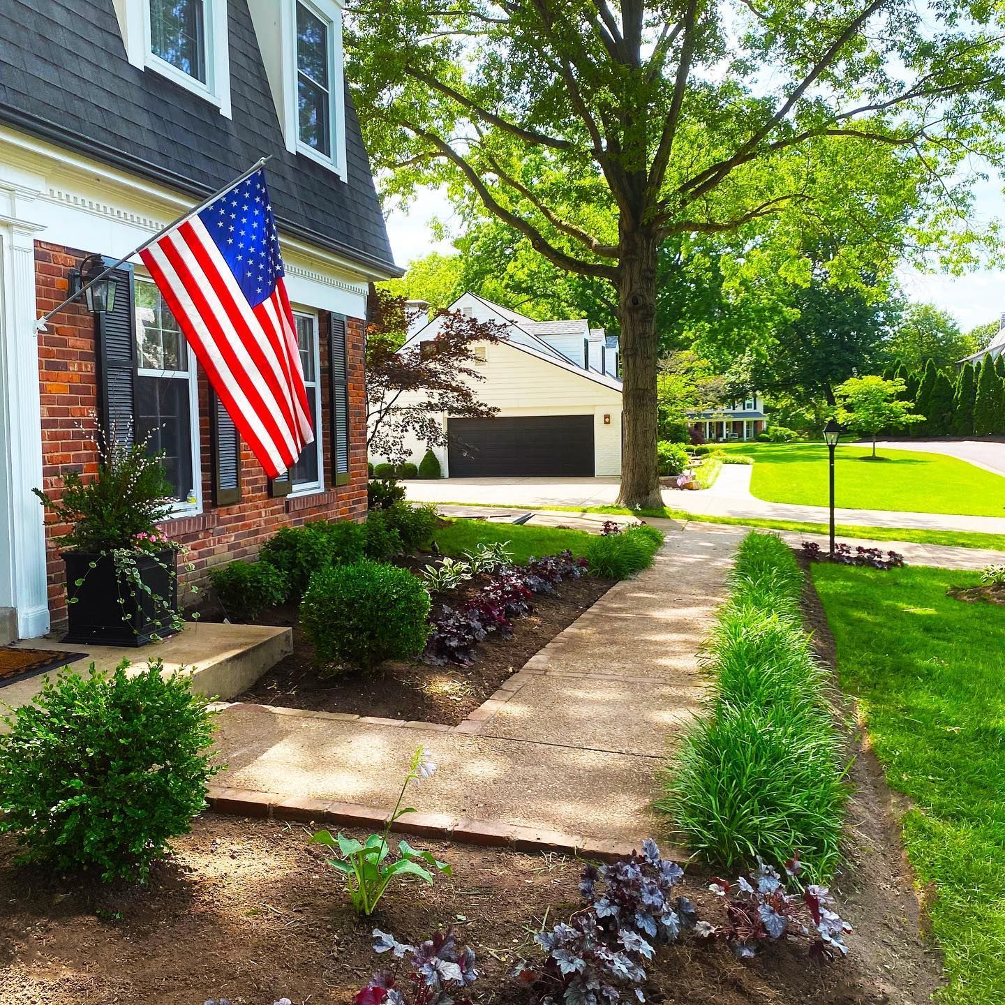 House with American flag, landscaped garden with a walkway and lush greenery.