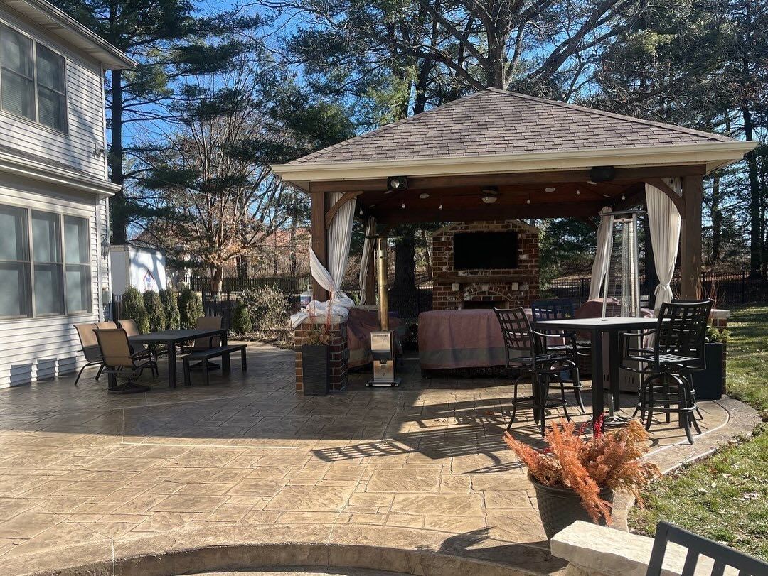 Backyard patio with a gazebo, seating, and a television. The stamped concrete patio has furniture
