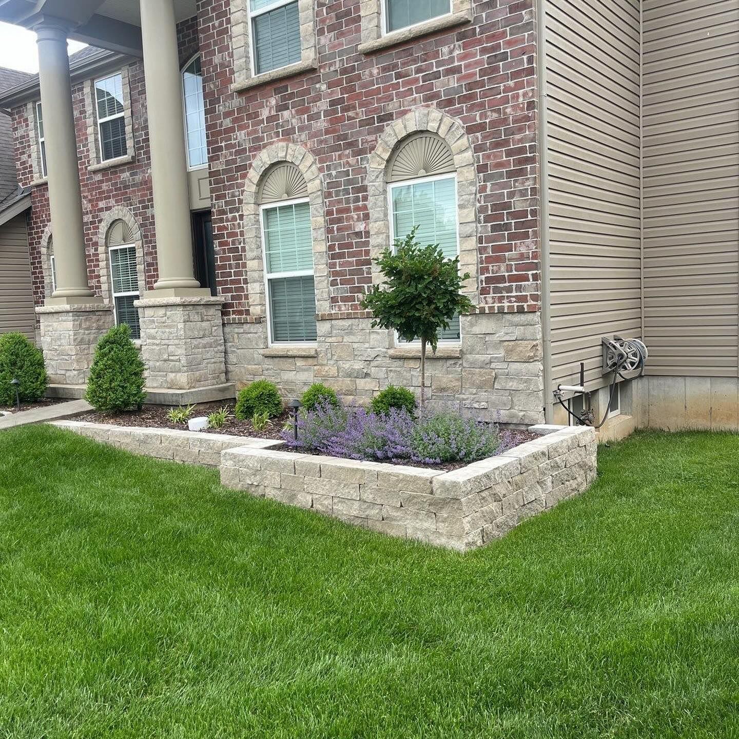 Brick house with a stone planter filled with lavender and small shrubs. Green lawn in the foreground.